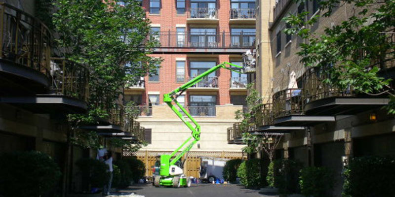 Painting contractor on green cherry picker working on building